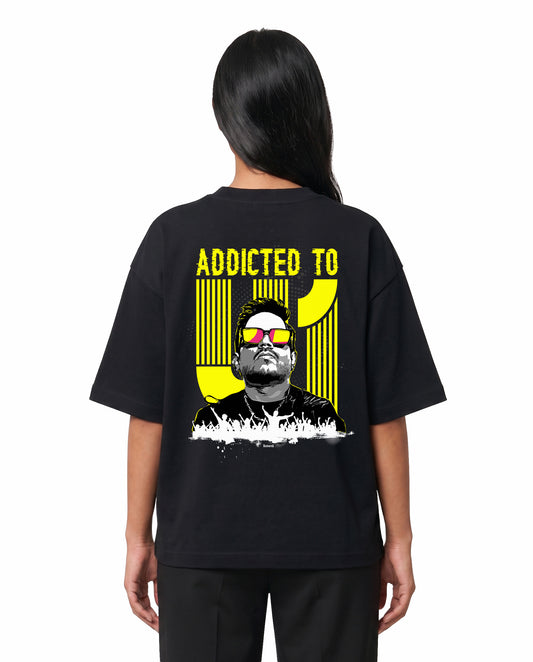 Back view of female model wearing ADDICTED TO U1 unisex oversized graphic t-shirt in black in a studio setting.