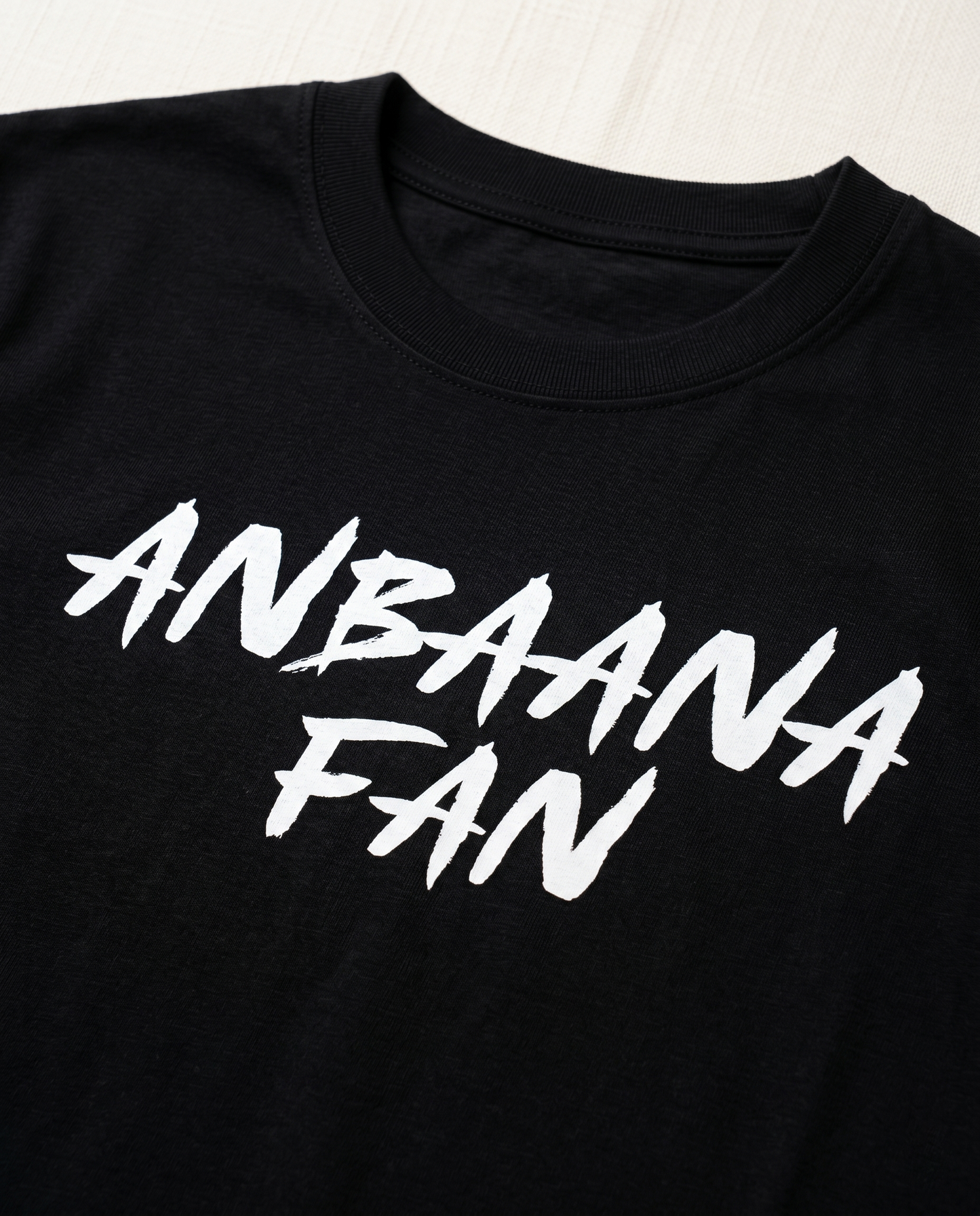 Close-up view of the ANBAANA FAN graphic print highlighting typography details and premium print quality on a black men's regular-fit t-shirt.