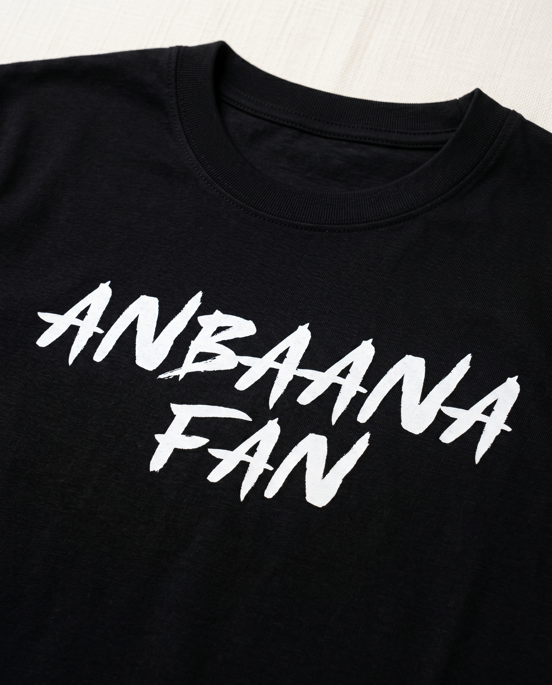 Close-up view of the ANBAANA FAN graphic print highlighting typography details and premium print quality on a black men's regular-fit t-shirt.