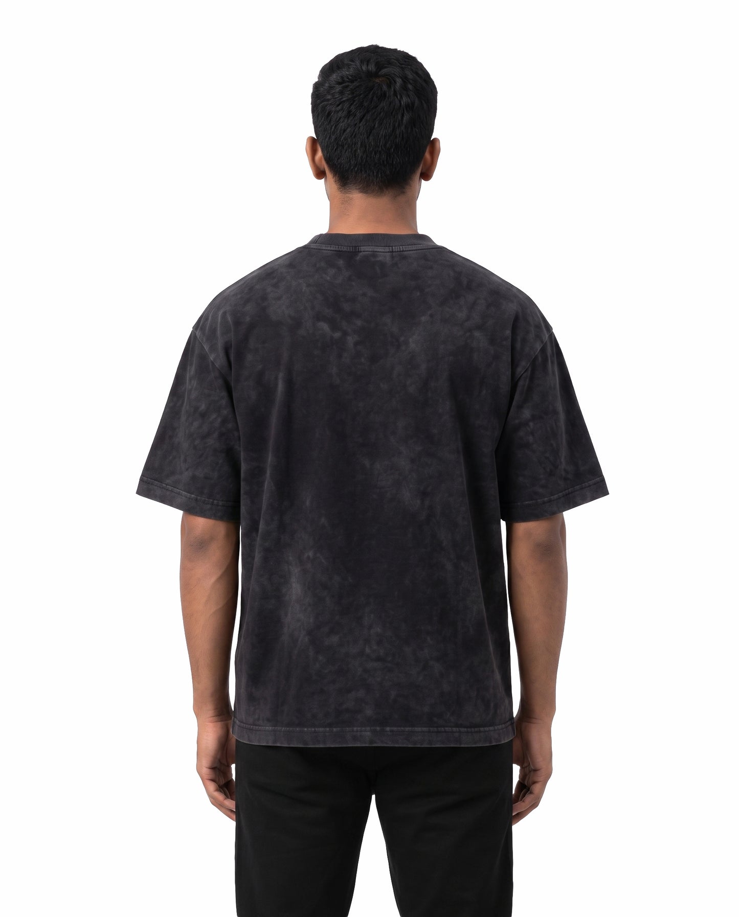 Back view of male model wearing BRO CODE unisex acid washed oversized graphic t-shirt in black in a studio setting.