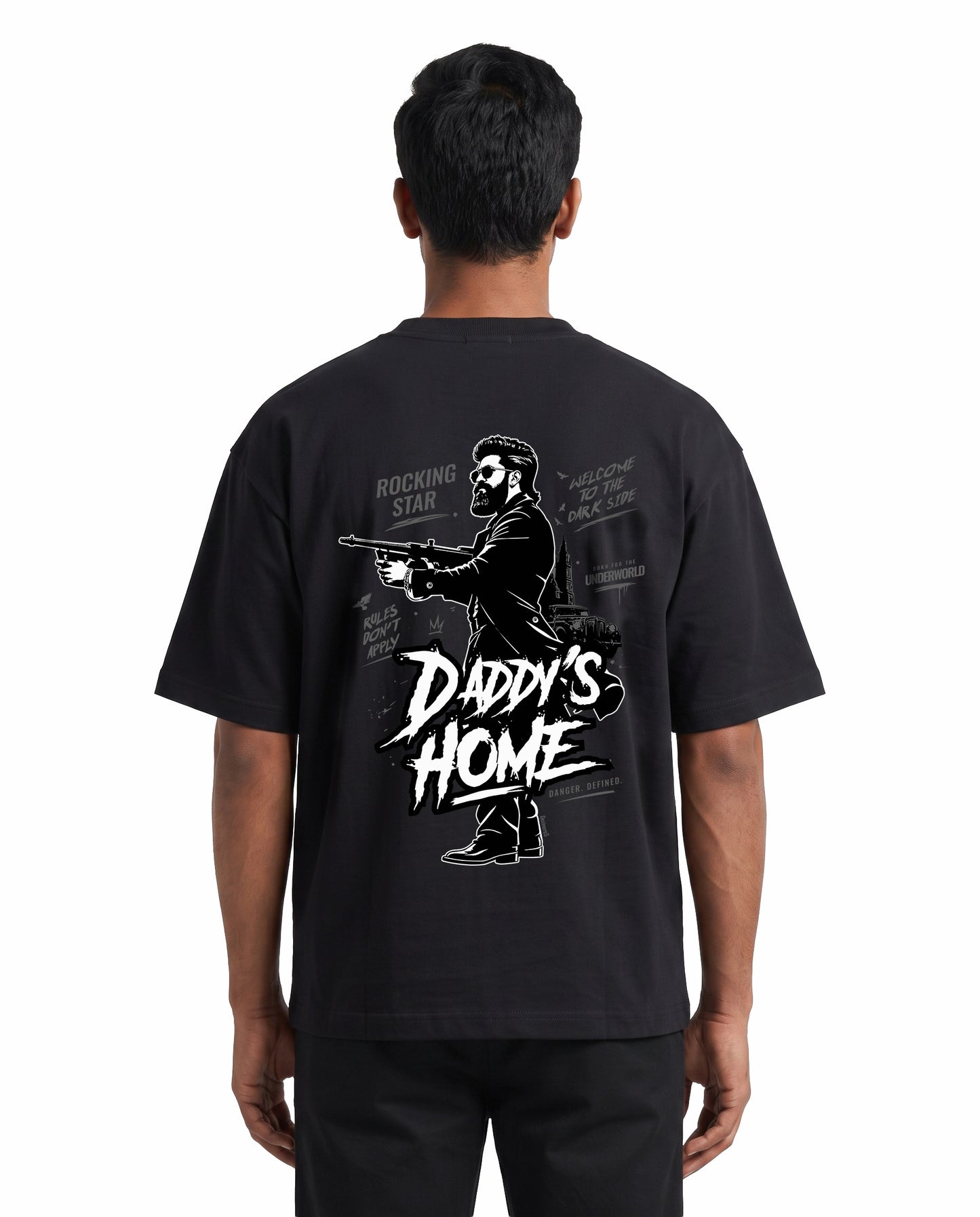 Back view of male model wearing DADDY'S HOME unisex oversized graphic t-shirt in black in a studio setting.