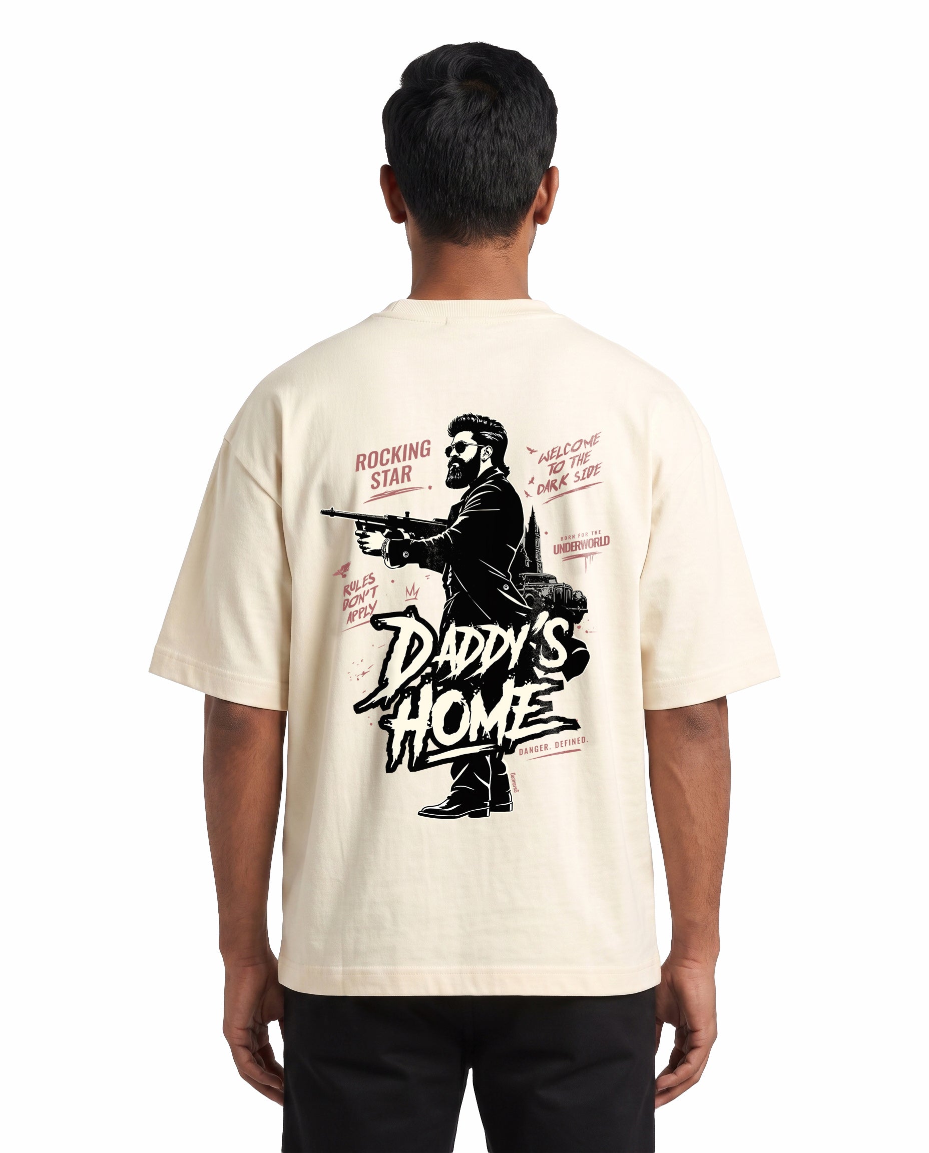 Back view of male model wearing DADDY'S HOME unisex oversized graphic t-shirt in off-white in a studio setting.