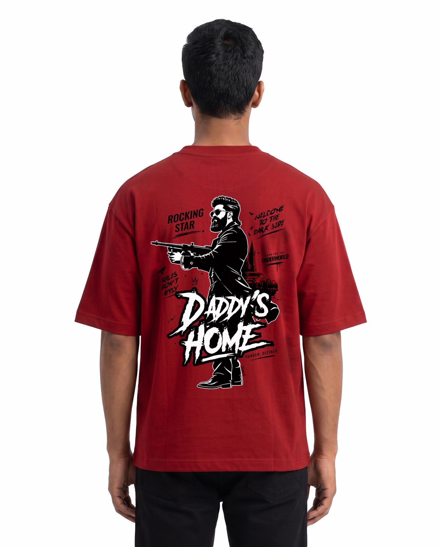 Back view of male model wearing DADDY'S HOME unisex oversized graphic t-shirt in red in a studio setting.