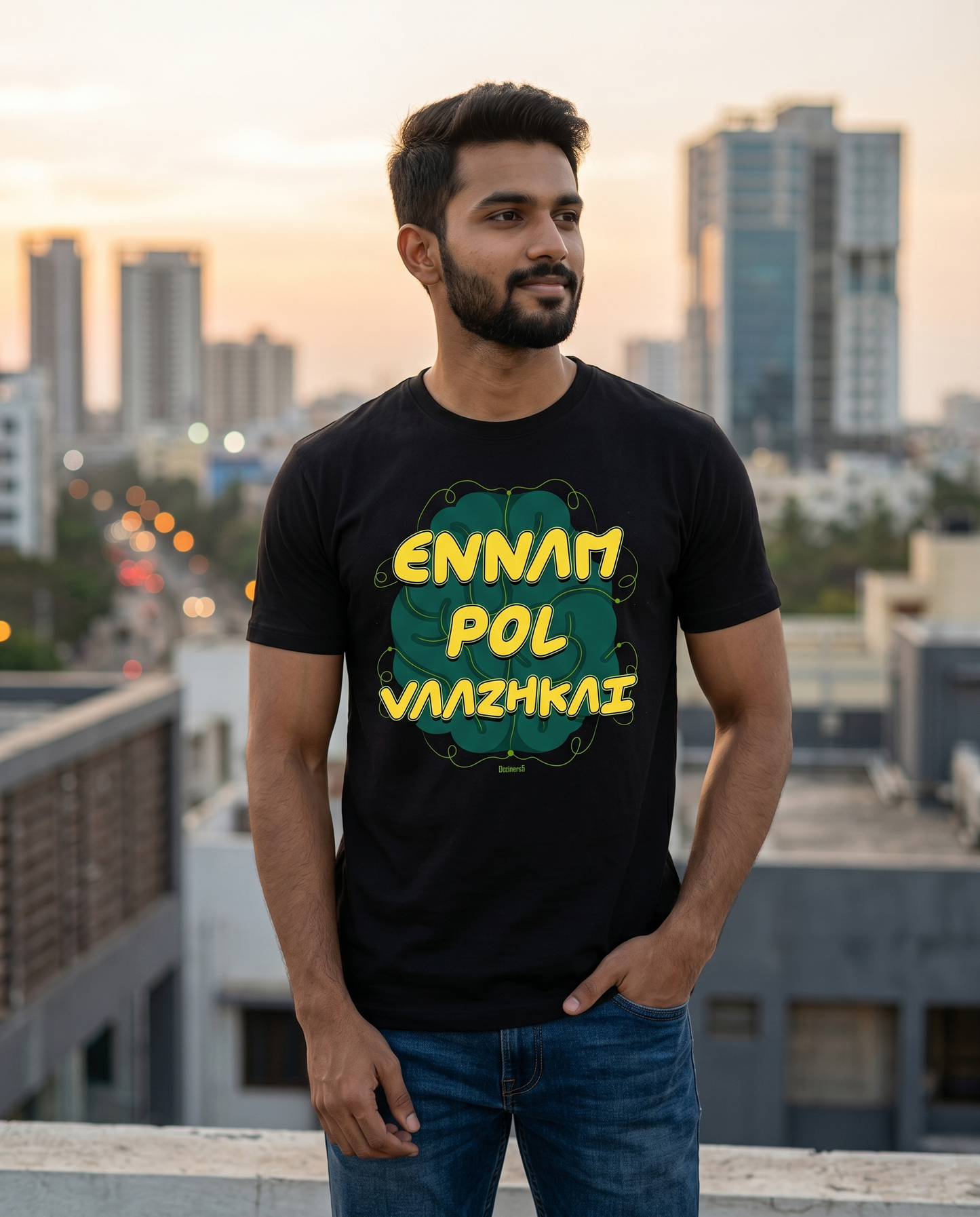 Young South Indian male wearing the ENNAM POL VAAZHKAI men's regular-fit t-shirt in black on a rooftop overlooking the Chennai skyline at sunset.