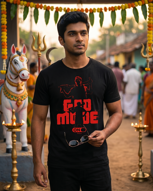 Young South Indian male wearing the GOD MODE men's regular-fit t-shirt in black near a traditional Tamil village guardian shrine.