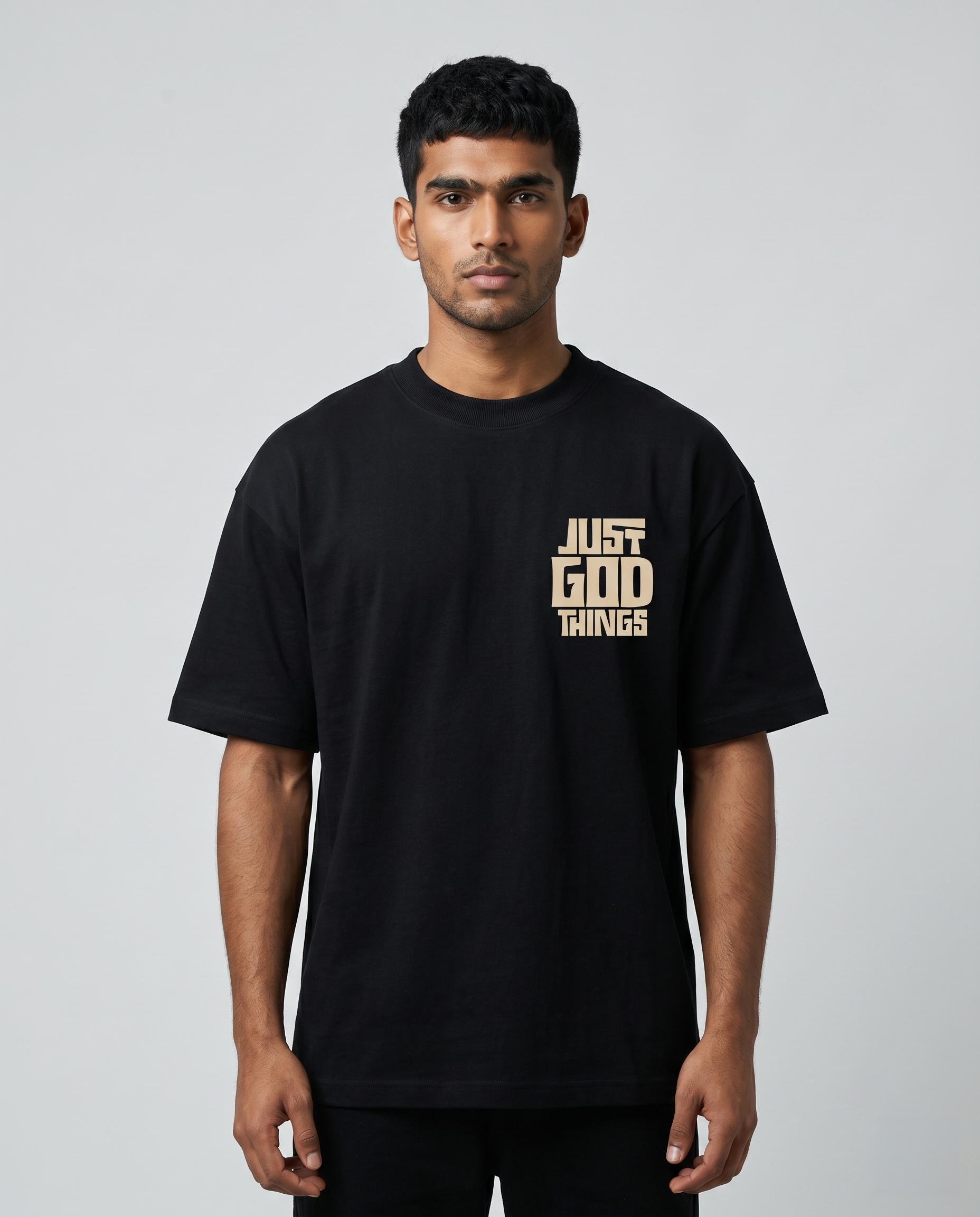 Man wearing a JUST GOD THINGS - Unisex oversized graphic t-shirt with text as a pocket chest print on a gray background.