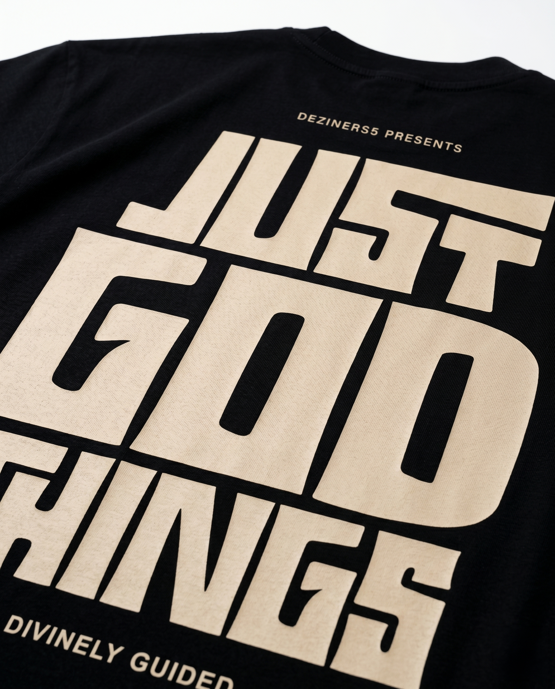Close up of JUST GOD THINGS - Unisex oversized graphic t-shirt print detail with beige text on a white background.