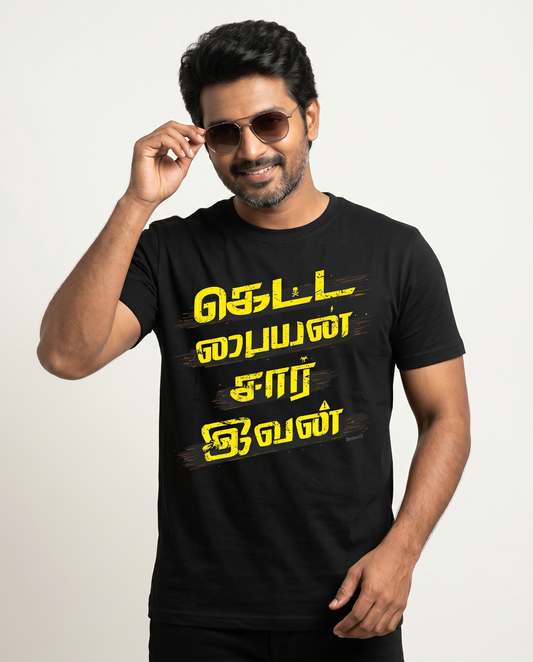 Young South Indian male wearing the KETTA PAIYAN men's regular-fit t-shirt in black in a premium studio lifestyle setting with confident superstar-inspired energy.