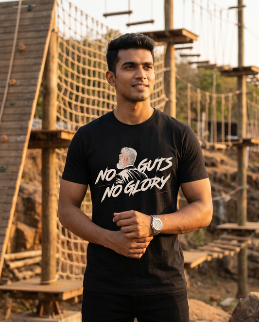 Young South Indian male wearing the NO GUTS NO GLORY men's regular-fit t-shirt in black at an outdoor adventure training ground.
