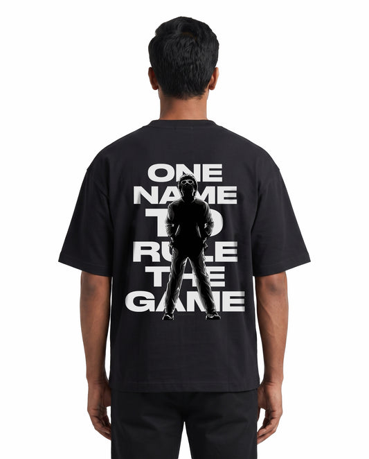 Back view of male model wearing ONE NAME unisex oversized graphic t-shirt in black in a studio setting.