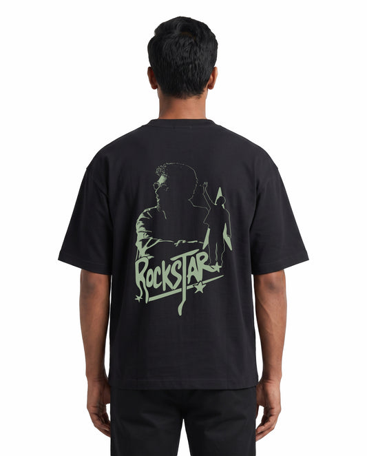 Back view of male model wearing ROCKSTAR - Unisex Oversized Graphic T-Shirt in black in a studio setting.