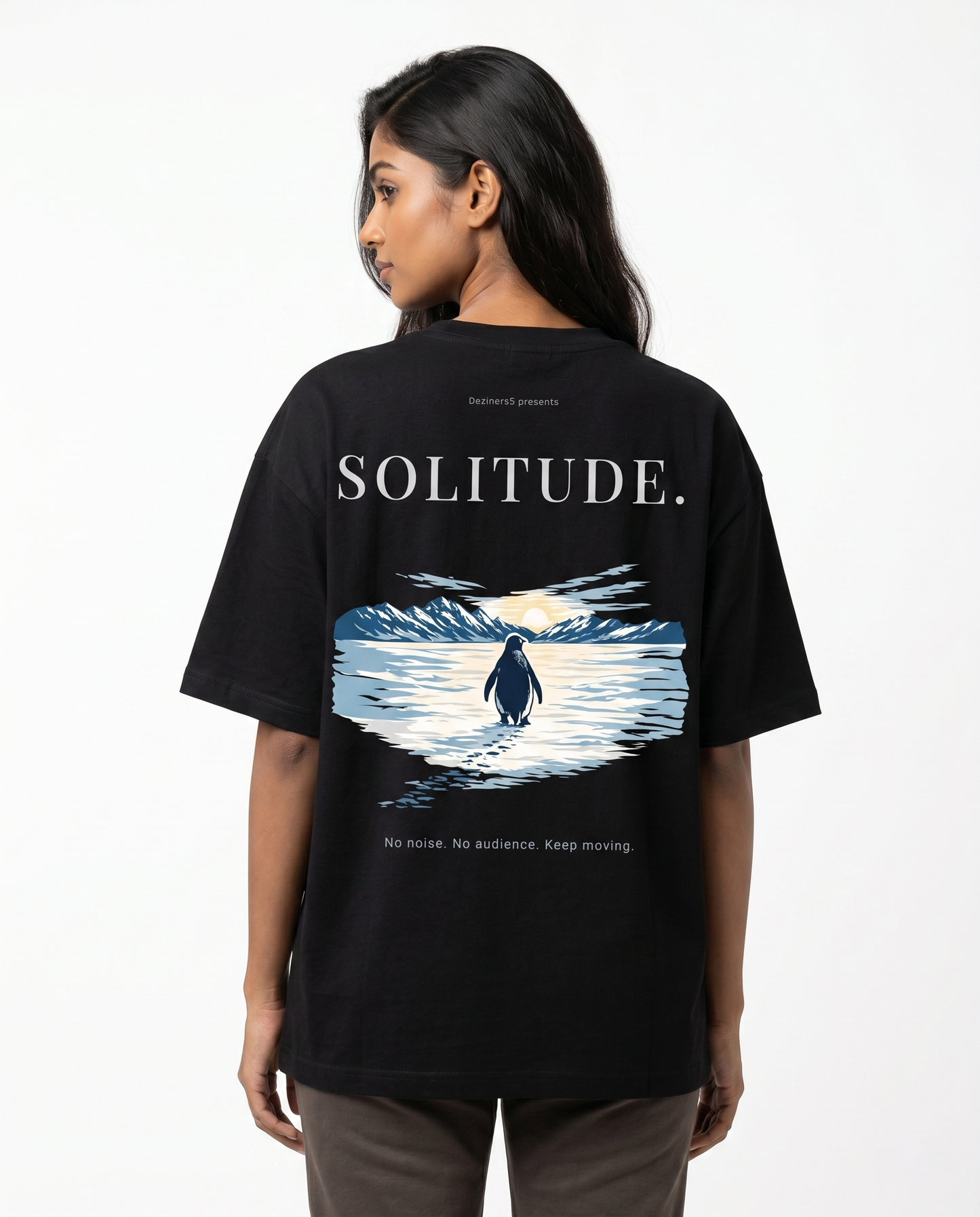 South Indian female model wearing the SOLITUDE - unisex oversized graphic t-shirt in black featuring large motivational penguin artwork on the back.