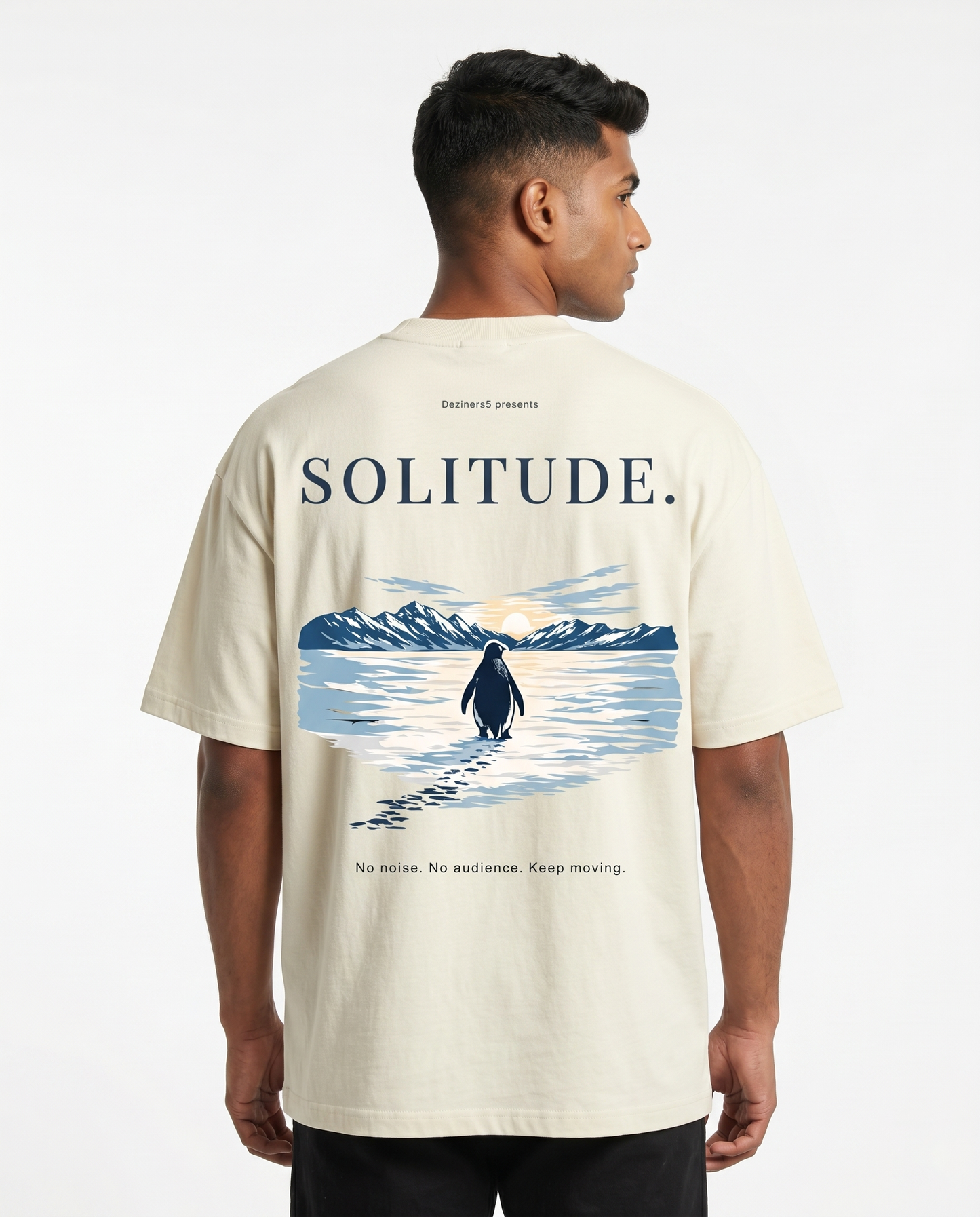 South Indian male model wearing the SOLITUDE - unisex oversized graphic t-shirt in off-white featuring large motivational penguin artwork on the back.