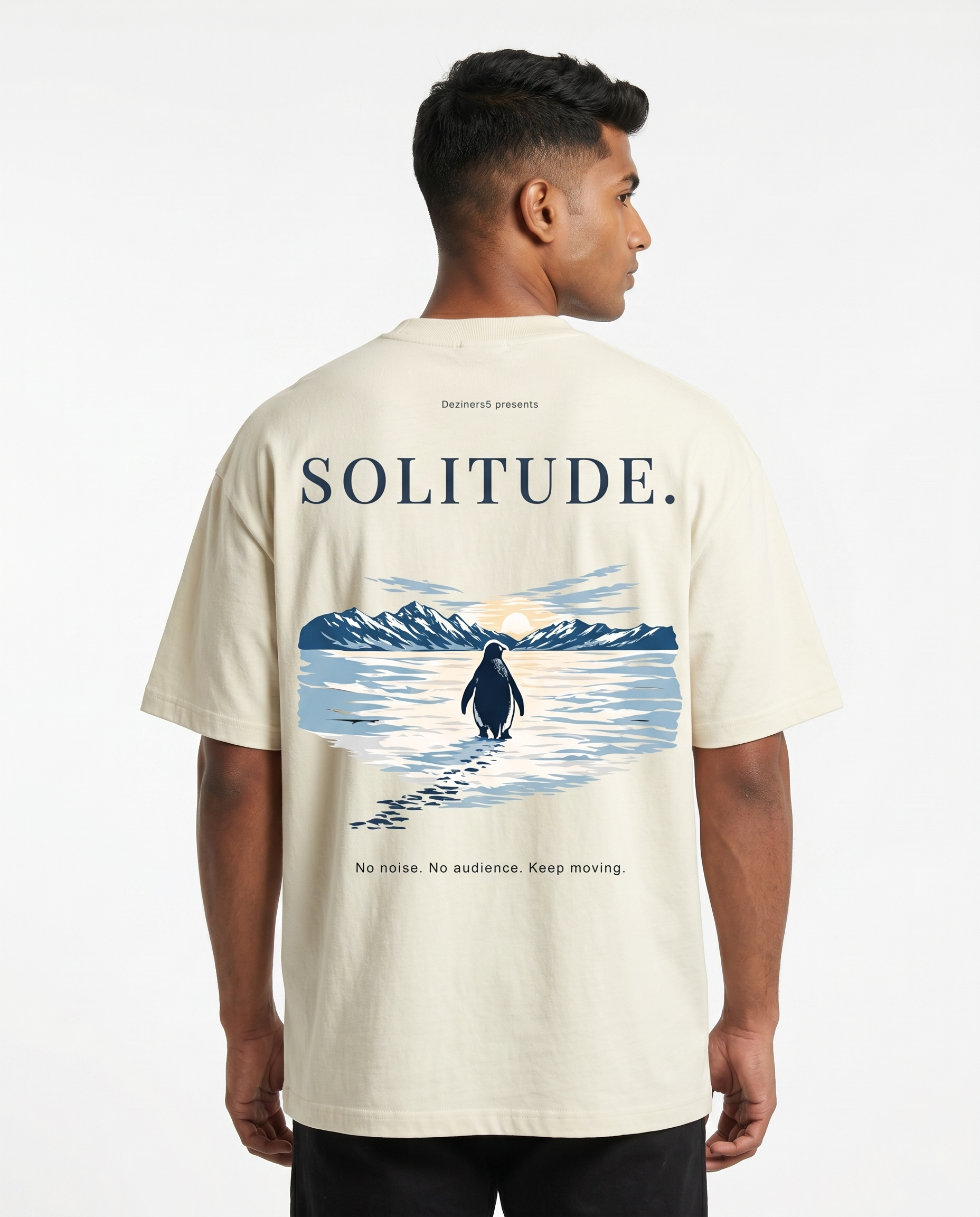 South Indian male model wearing the SOLITUDE - unisex oversized graphic t-shirt in off-white featuring large motivational penguin artwork on the back.