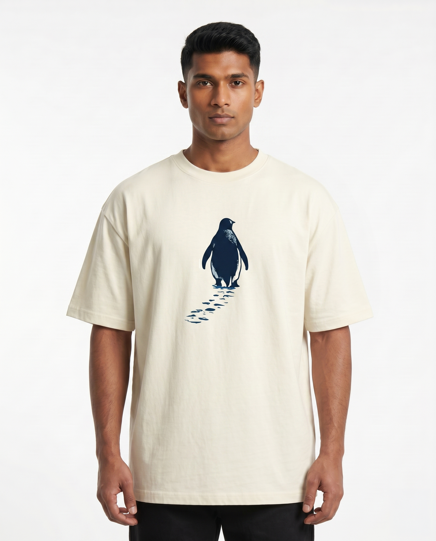 South Indian male model wearing the SOLITUDE - unisex oversized graphic t-shirt in off-white featuring a minimalist penguin chest graphic.