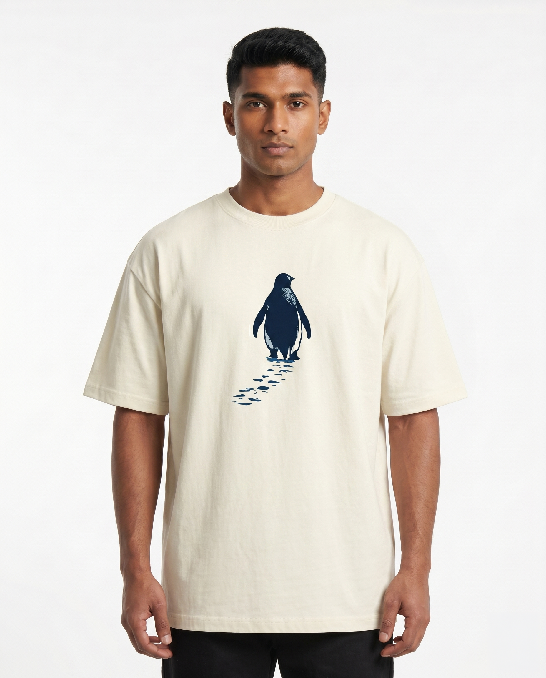 South Indian male model wearing the SOLITUDE - unisex oversized graphic t-shirt in off-white featuring a minimalist penguin chest graphic.